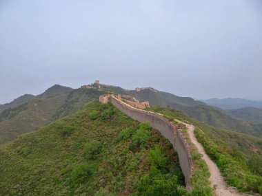 A panoramic view on an unrenewed Gubeikou part of Great Wall of China. The wall is spreading on tops of mountains. Many watchtowers on the peaks. Dense forest around it. World wonder. Tradition