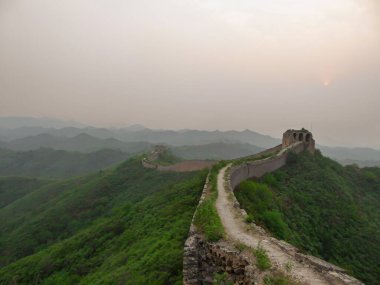 A panoramic view on an unrenewed Gubeikou part of Great Wall of China. The wall is spreading on tops of mountains. Many watchtowers on the peaks. Dense forest around it. World wonder. Tradition