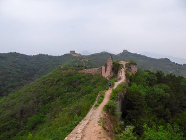 A panoramic view on an unrenewed Gubeikou part of Great Wall of China. The wall is spreading on tops of mountains. Many watchtowers on the peaks. Dense forest around it. World wonder. Tradition