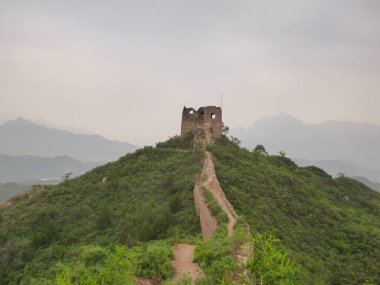 A panoramic view on an unrenewed Gubeikou part of Great Wall of China. The wall is spreading on tops of mountains. Many watchtowers on the peaks. Dense forest around it. World wonder. Tradition