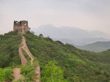 A panoramic view on an unrenewed Gubeikou part of Great Wall of China. The wall is spreading on tops of mountains. Many watchtowers on the peaks. Dense forest around it. World wonder. Tradition