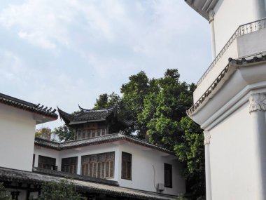 A white building in Chinese style build in Fuzhou, China. There are dense trees behind the building. Overcast with a few sun rays coming through. Housing residency