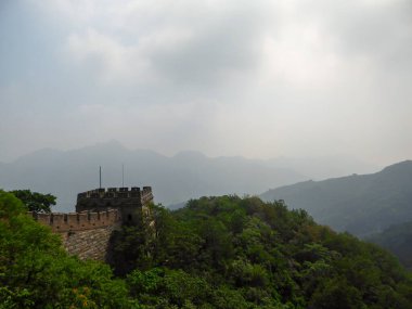 A panoramic view on a renewed Jinshanling part of Great Wall of China. The wall is spreading on tops of mountains. Many watchtowers on the peaks. Dense forest around it. World wonder. Tradition
