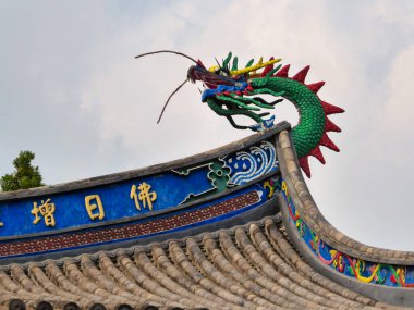 A close up on the richly decorated rooftop of a temple in Fuzhou, China. There is a colorful head of the dragon, guarding the temple from bad spirits. Few clouds on the sky. Spirituality and tradition