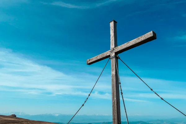 A wooden cross on top of Sauofen in Austrian Alps. Fall vibes. Mountain chains in the back. Panoramic view. There are a few white clouds on the sky. Achievement and spirituality