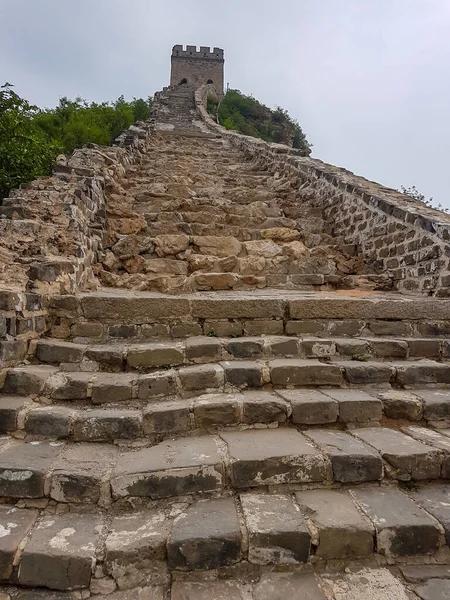 A steep staircase to the watchtower on the old part of Great Wall Jinshanling in China. The wall is spreading on tops of mountains. Thick and dense forest on the slopes. World wonder. Air pollution