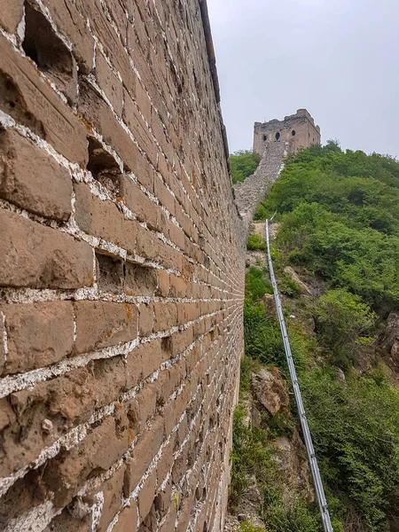 A side view on the old part of Great Wall Jinshanling in China. The wall is spreading on tops of mountains, with watchtowers on top. Thick and dense forest on the slopes. World wonder. Air pollution