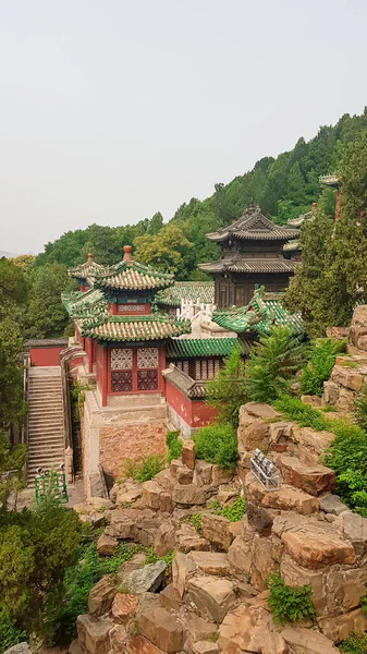 A panoramic view on a buildings complex in park of Summer Palace in Beijing, China. The buildings are richly decorated with gold. Few trees grow around. A bit of overcast due to the air pollution