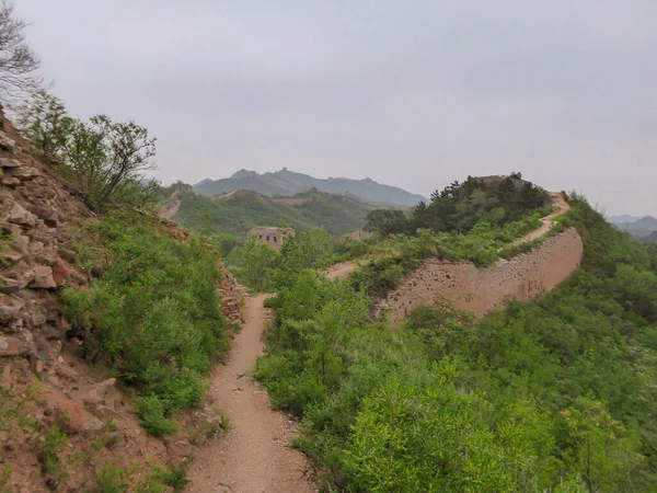 A panoramic view on an unrenewed Gubeikou part of Great Wall of China. The wall is spreading on tops of mountains. Many watchtowers on the peaks. Dense forest around it. World wonder. Tradition