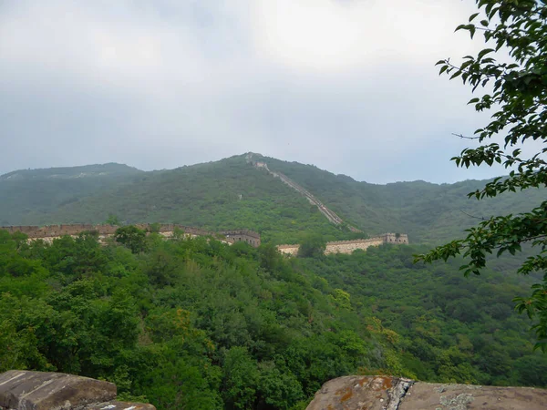 A panoramic view on a renewed Jinshanling part of Great Wall of China. The wall is spreading on tops of mountains. Many watchtowers on the peaks. Dense forest around it. World wonder. Tradition