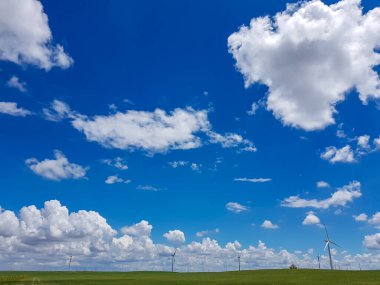 A field of wind turbines build on a vast pasture in Xilinhot in Inner Mongolia. Natural resources energy. Clean energy. Endless grassland. Blue sky with white, thick clouds. Serenity