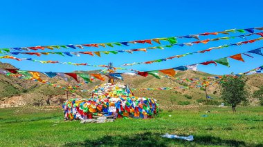 A big white heap of stones (aobao) with panoramic view on Daqing mountains in Inner Mongolia. It has a few colorful prayer flags attached to it and waving around it. Desolated landscape. Spirituality