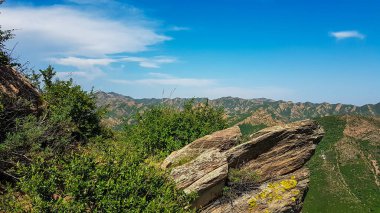 A panoramic view on Daqing mountains in Inner Mongolia. Endless mountain chains. The slopes are overgrown with small bushes and grass. Desolated landscape. Clear and sunny. Bio diversity of a region