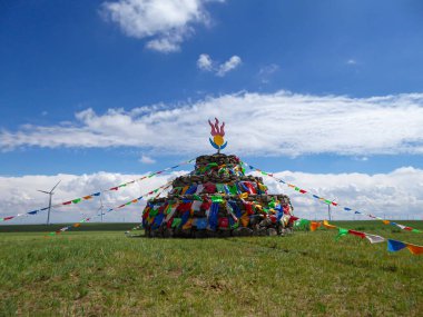 Heaps of stones (Aobao) build on a vast pasture in Xilinhot in Inner Mongolia. The Heaps has a lot of colorful prayer flags attached to it. Endless grassland. Blue sky with white clouds. Religious place