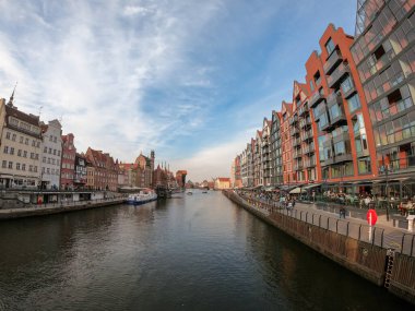A panoramic view on the shores of Martwa Wisla flowing through Gdansk in Poland, with medieval port crane. New architecture meeting with medieval constructions. Sunny day. Calm water. City tour