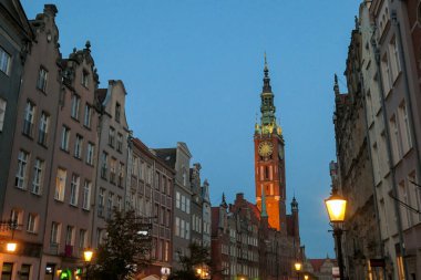 A close up of the facades of tall building in the middle of Old Town in Gdansk, Poland. The buildings have many bright colors, they are richly decorated. High tower of Town Hall. Sightseeing at night