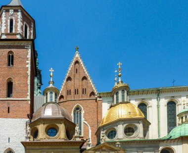 A close up on the rooftops of Wawel Castle in Cracow, Poland. The rooftops are richly decorated with gold and some small figures. Clear and blue sky above the city.