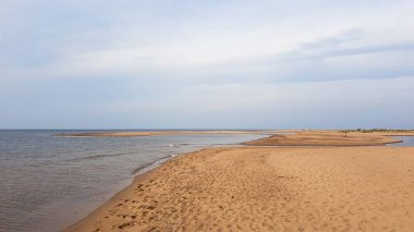 Footsteps left on the shore of a sandy beach by Baltic Sea on Sobieszewo island, Poland. The sea is gently waving. A bit of overcast. Walking barefoot. Endless horizon line.