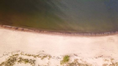 A top down drone shot of the sandy beach by the Baltic Sea on Sobieszewo island, Poland. The waves are gently rushing to the shore. The beach is overgrown with some bushes and grass. Waves meditation