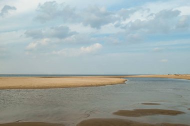 The coastal line of a sandy beach by the Baltic Sea on Sobieszewo island, Poland. There is a small pond separated from the sea by sand dunes. A bit of overcast. Endless horizon. Solitude and calmness.
