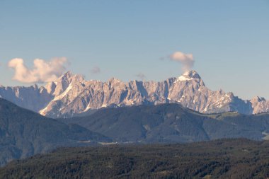 A close up view on Dobratsch, a mountain in Austrian Alps. The mountain's sides are baren and sharp. High mountaineering. Clear and blue sky, with a few clouds above the peaks. Calmness.
