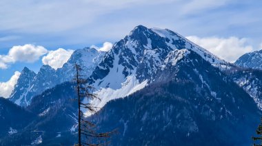 A panoramic view on high Alpine chains in Austria, partially covered with snow. Early spring in the mountains. The slopes are baren and very steep. Few clouds between the peaks. Calmness and freedom