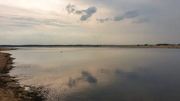 A panoramic view on a small lake along the Baltic Sea. The lake is separated from the sea by a sand dune. The clouds are reflecting in the calm surface of the lake. Calmness and serenity