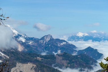 A panoramic view from the top of Alpine peak in Austria. The whole area is shrouded in thick clouds. A few peaks popping out from the clouds. High mountain chains in the back. Carpet from the clouds