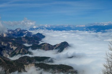 A panoramic view from the top of Alpine peak in Austria. The whole area is shrouded in thick clouds. A few peaks popping out from the clouds. High mountain chains in the back. Carpet from the clouds