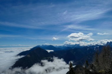 A panoramic view from the top of Alpine peak in Austria. The whole area is shrouded in thick clouds. A few peaks popping out from the clouds. High mountain chains in the back. Carpet from the clouds