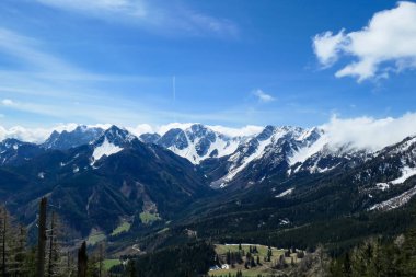 A panoramic view on Baeren Valley in Austrian Alps. The highest peaks in the chain are sonw-capped. Lush green pasture in front. A few trees on the slopes. Clear and sunny day. High mountain chains.