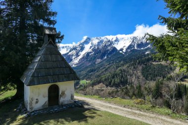 A small chapel with a panoramic view on Baeren Valley in Austrian Alps. The highest peaks in the chain are sonw-capped. Lush green pasture in front. Clear and sunny day. High mountain chains.