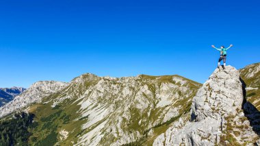 A woman with a hiking backpack standing on top of a big boulder on the way to Hohe Weichsel in Austria, with a panoramic view on a vast valley. The woman in enjoying the calmness and peace. Exploration