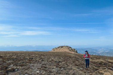 A woman with hiking backpack walking from the top of Sauofen in Austrian Alps. She is walking through a vast, golden pasture. Fall vibes. Mountain chains in the back. Serenity and achievement