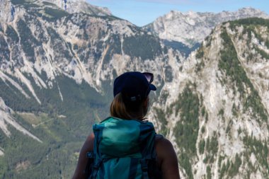 A woman with a hiking backpack admiring the view on the Alpine mountain chains in Austria, Hochschwab region. The slopes are partially overgrown with small bushes, higher parts baren. Happiness