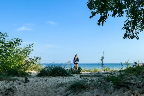一位穿着短裤的妇女站在一条小河的汇合处 来到波兰的波罗的海 沙滩上长满了矮树丛 后面是一片平静的大海 发现和探索 — 图库照片