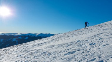 A man wearing snow shoes hiking up along a steep slope to the peak of Speikkogel in Austrian Alps. The whole slope is covered with snow. many mountain chains in the back. Winter outdoor activity.