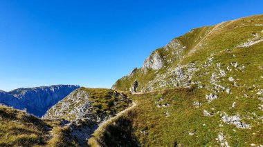 A man with a hiking backpack hiking along a narrow pathway to the top of Hohe Weichsel in Austria. The man in enjoying the calmness and peace. Lush green pasture around him. Exploration and discovery