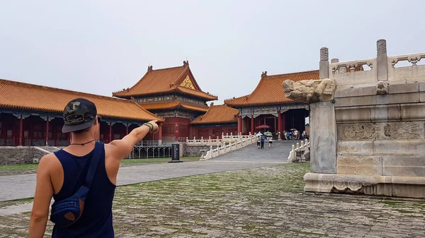 一位男子站在中国北京紫禁城的广场上 他指着面前的一个巨大的门 旁边有一个很长的亭子 发现旅游的地方 — 图库照片