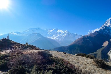 White stupa standing on mountain peak, with high, snow caped Himalayas in the back, Annapurna Circuit Trek, Nepal. Sharp and steep slopes of the mountain. First sunbeams reaching the peak. Meditation