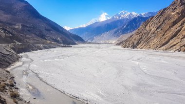 A view on a dry bottom of Himalayan valley. The valley is located in Mustang region, Annapurna Circuit Trek in Nepal. In the back there is snow capped Dhaulagiri I. Barren and steep slopes