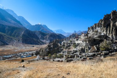 A temple complex in Manang Annapurna Circuit Trek, Nepal. Stupa in front of other buildings. Temple built on a rocky mountain hills. Sacred place for many Buddhist tourists. Dry land. Clear sky.