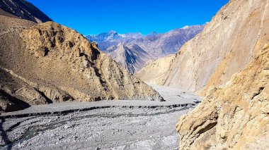 A small stream flowing in the dry bottom of Himalayan valley. The valley is located in Mustang region, Annapurna Circuit Trek in Nepal. Barren and steep slopes. HArsh landscape.
