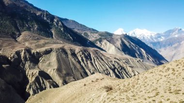 A panoramic view on dry Himalayan landscape. Located in Mustang region, Annapurna Circuit Trek in Nepal. In the back there is snow capped Dhaulagiri I. Barren and steep slopes. Harsh condition.