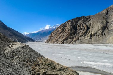 A panoramic view on dry Himalayan landscape. Located in Mustang region, Annapurna Circuit Trek in Nepal. In the back there is snow capped Dhaulagiri I. Barren and steep slopes. Harsh condition.