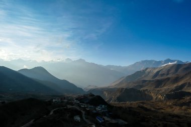 Himalayan chains shrouded in fog, seen from Muktinath, Annapurna Circuit Trek, Nepal. There are multiple mountain chains. Sunbeams breaching through the peaks. Golden hour. Meditation and serenity.