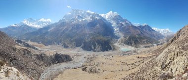 A panoramic view on Manang valley from Praken Gompa, Nepal. High Himalayan ranges around. There is a small lake in the valley. Snow capped peaks of Annapurna Chain. Harsh landscape.