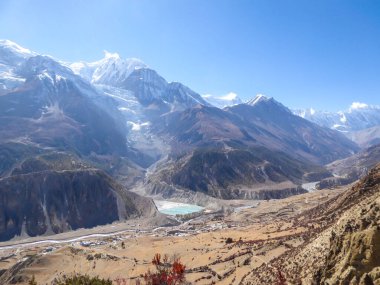 A panoramic view on Manang valley from Praken Gompa, Nepal. High Himalayan ranges around. There is a small lake in the valley. Snow capped peaks of Annapurna Chain. Harsh landscape.