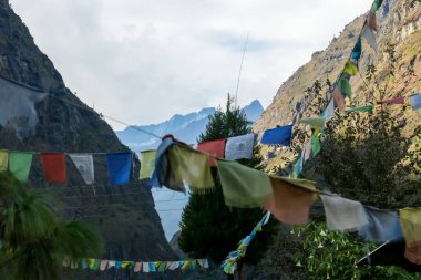 A few lines of prayer flags waving on the wind in Himalayan village, Tal, Nepal, along Annapurna Circuit Trek. There are high mountain chain around. Spirituality and meditation.
