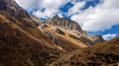 Harsh and golden colored slopes in Manang Valley, Annapurna Circus Trek, Himalayas, Nepal, with the view on Annapurna Chain and Gangapurna. Dry and desolated landscape. High snow capped mountain peaks